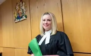 A judge holds files in front of the official provincial crest and smiles
