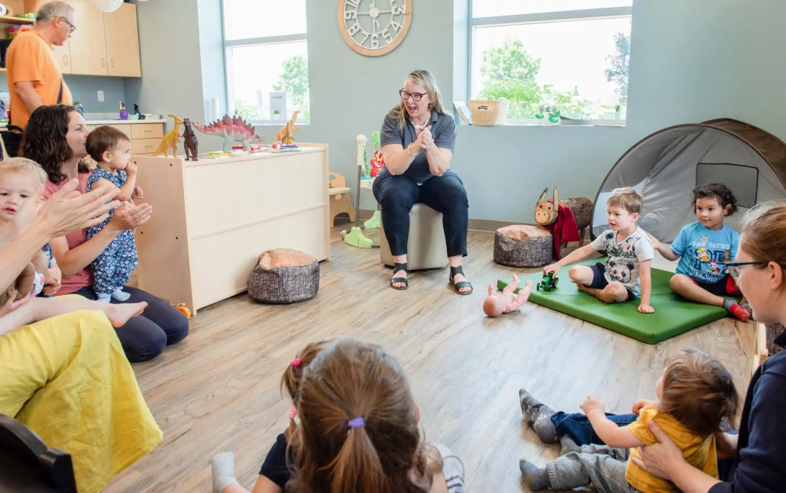 EarlyON educator sings and dances in a circle with children and caregivers